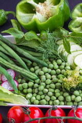 A set of vegetables: peas, green pepper, radishes, cucumber. Black background.