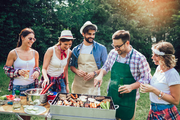 Young friends having fun grilling meat enjoying barbecue party.