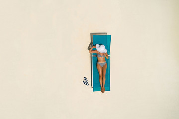 Aerial view of slim woman sunbathing lying on a beach chair in Maldives. Summer seascape with girl....