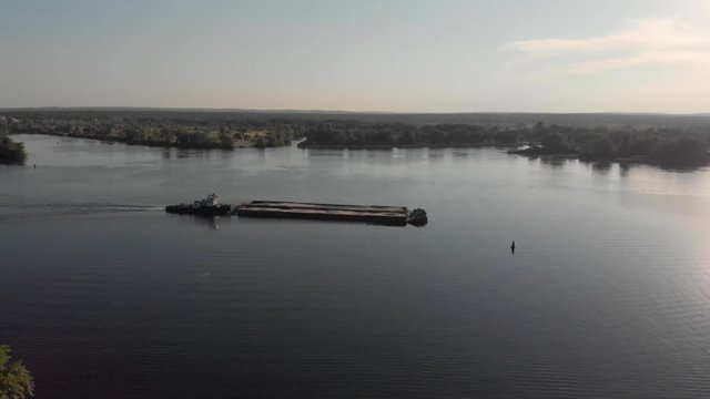 Barge ship towing sand cargo on large river at sunset aerial backlit