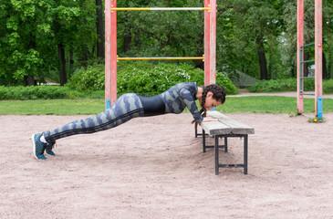 girl in sports clothes doing push-UPS from a bench in the Park against the background of greenery