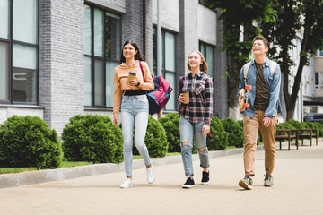 smiling teenagers walking, holding disposable cups, looking away