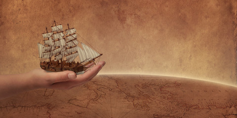 Old sailing ship in hand concept. Retro world map and globe in background.