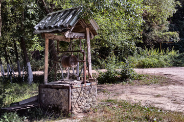 Abandoned old rusty well under covered cabin with a collar, drum and chain.