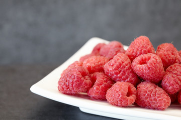 a plate of  raspberry on a dark stone background, natural berry with natural backlight on black...