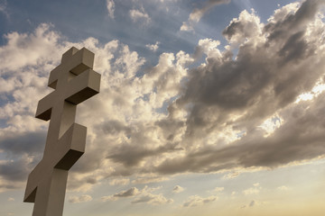 Cross on the background of storm clouds with glimpses of the sun's rays through them and the blue sky, a dramatic view