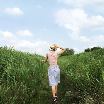 A girl in a hat running through a high grass