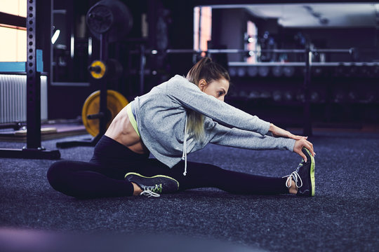 Side profile of young woman sitting and stretching on the floor at fitness centre