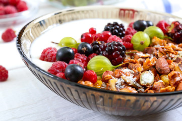 Yogurt, granola, fresh berries in a bowl on a white wooden background. Delicious and healthy breakfast. Proper nutrition. Dietary menu.