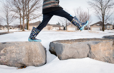 Cropped image of a boy's legs taking big step across large rocks.