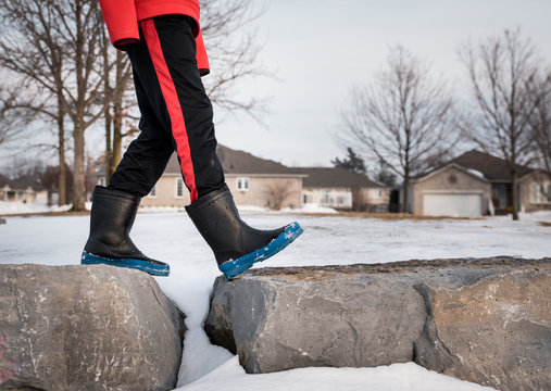 Cropped image of boy's lower half walking across large rocks in boots.