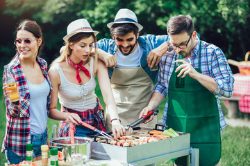 Young friends having fun grilling meat enjoying barbecue party.