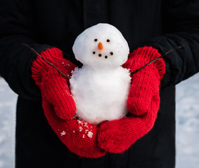 Close up of hands in red wool mittens holding a small snowman.