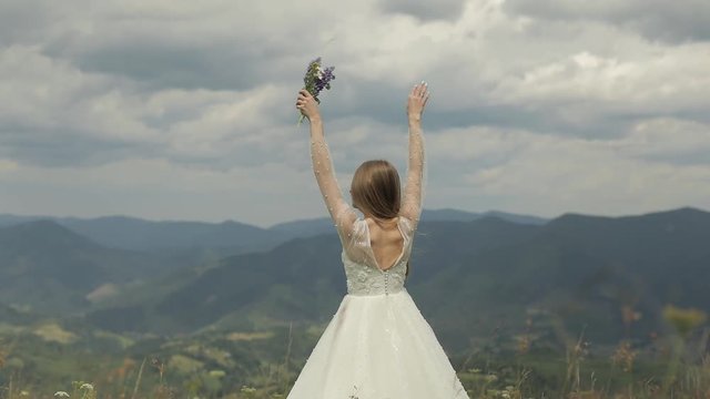 Beautiful bride in wedding dress stay on the mountains with bouquet of flowers