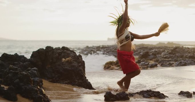 Beautiful polynesian woman performing a Tahitian hula dance on the beach in slow motion at sunset with the ocean moving in the background