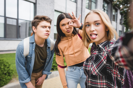 positive teenagers taking selfie and showing ok gesture outside