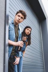 boy and brunette teenager looking away, smoking cigarette and drinking beer