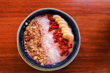 Plate with summer breakfast, fruit salad on a brown table. Fruit and nut breakfast - sweet mousse decorated with sliced bananas, almonds, coconut flakes, nuts.