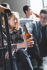 smiling teenagers sitting on stairs, holding beer and talking