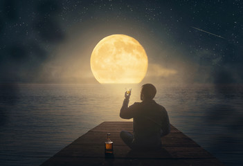 Man drinking whiskey and looking at the moon by the sea
