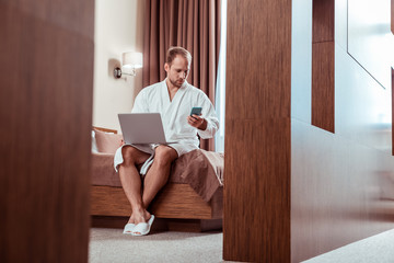 Focused man in comfortable hotel outfit sitting on the bed