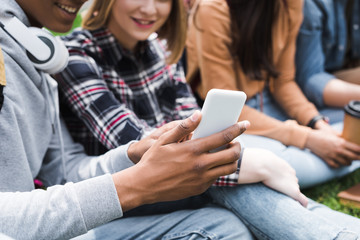cropped view of smiling and happy teenagers looking at smartphone