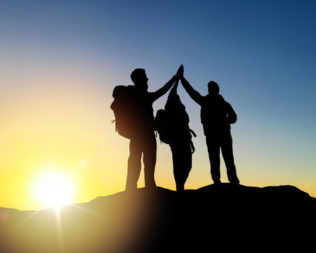 travel, tourism and hike concept - group of travelers with backpacks making high five on mountain top over sunrise background