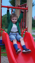 Fototapeta na wymiar Little boy having fun on a playground outdoors in summer. Toddler on a slide.