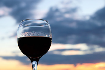 Glass with red wine on beautiful sunset background with colorful clouds. Concept of celebration, evening at resort, romantic dinner outdoors