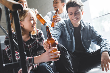 smiling teenagers sitting on stairs, drinking beer and talking