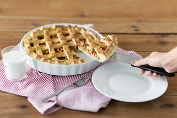 food, culinary and baking concept - close up of hand with piece of apple pie on knife