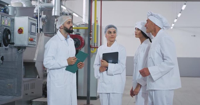 Baker chef old man and young engineer guy with beard have a conversation with their assistance in the middle of bakery industry factory