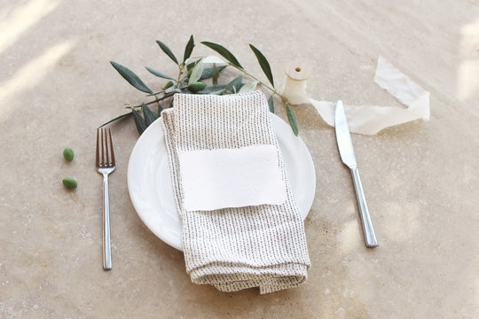 Festive Table Summer Setting With Silver Cutlery, Olive Branch, Porcelain Plate, Linen Napkin. Place Card Mockup. Marble Background In Sunlight. Mediterranean Wedding Or Restaurant Menu Concept.