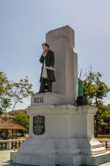 Puerto Princesa, Palawan, Philippines - March 3, 2019: Iwahig Penal Colony. Statue of independence hero Jose Rizal shows the man on gray concrete pedestal. Green foliage and blue sky.