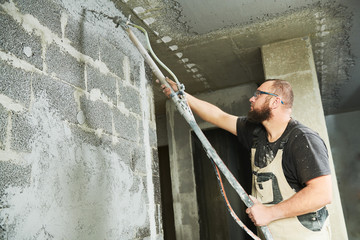 Plasterer using screeder spraying putty plaster mortar on wall