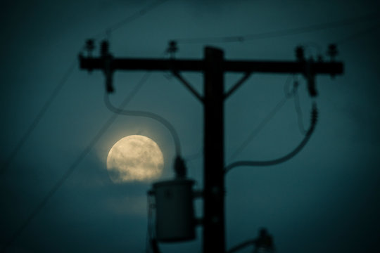 A full moon framed in a power line transformer