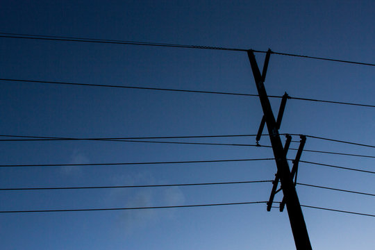 A silhouetted electricity power pole with transmission lines.