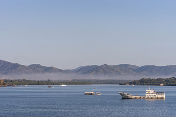 Obraz premium Puerto Princesa, Palawan, Philippines - March 3, 2019: The bay in front of the city shows blue water and brown mountains coverd in a light haze in the distance. Few boats. Light blue sky.