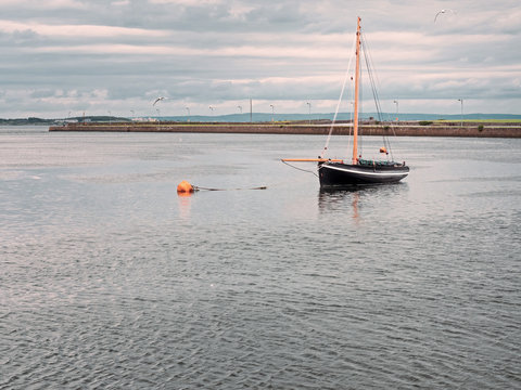 Traditional old wooden sailing boat in Galway bay. Black hull and orange mast, classic color.
