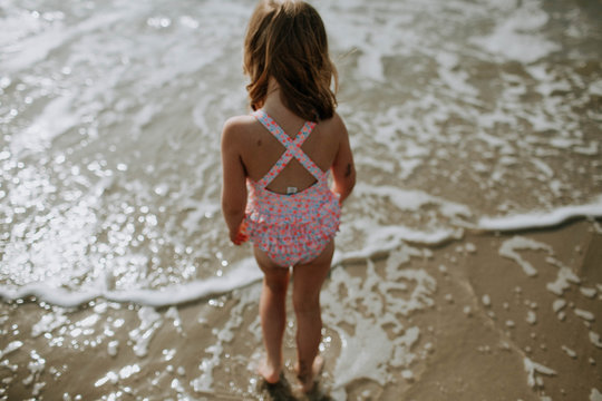 young girl walking into the ocean, shot from behind