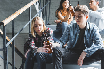 teenagers sitting on stairs, holding glass bottles and talking