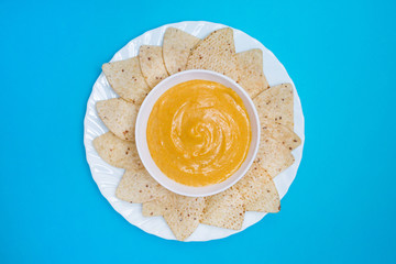 Queso cheddar vegano en un bol con nachos para mojar sobre un fondo azul.