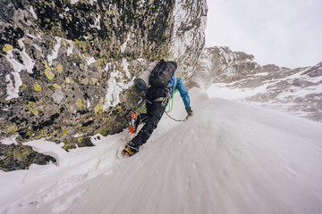An alpinist or a climber ascending steep snow alpine wall in harsh weather. Alpine mountauner climbing snow gully. Solo climber in winter High Tatras, Slovakia.