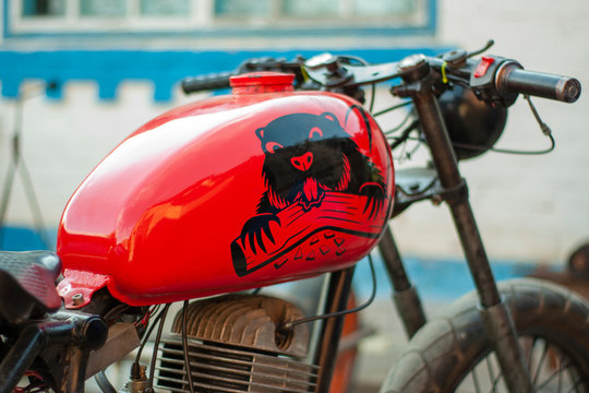 Old renovated red-colored motorcycle with a beaver stick on a tank.
