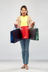 sale, outlet and consumerism concept - amazed asian young woman with shopping bags over grey background