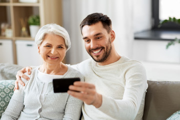 family, generation and people concept - happy smiling senior mother with adult son taking selfie by smartphone at home