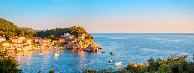 Schilderijen op glas Picturesque summer view of Adriatic sea coast in Budva Riviera. Przno village with buildings on the rock at sunset warm sunlight, Montenegro © O.Farion