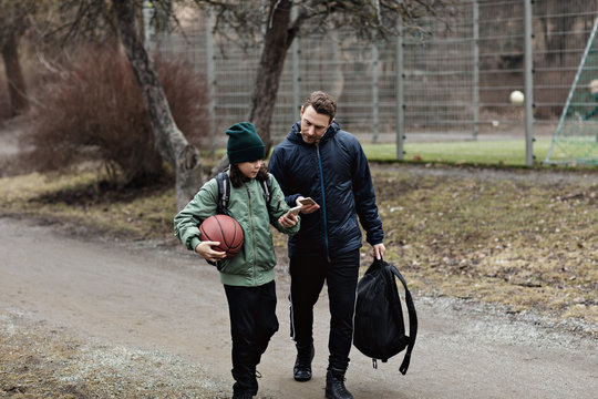 Father and son using mobile phones while walking on street during winter