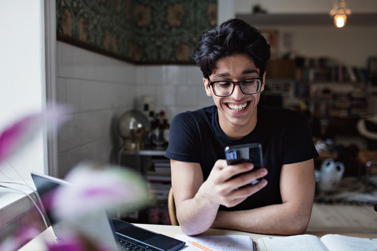 Smiling young man using smartphone at home