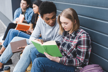 african american and caucasian teenagers sitting, talking and reading book